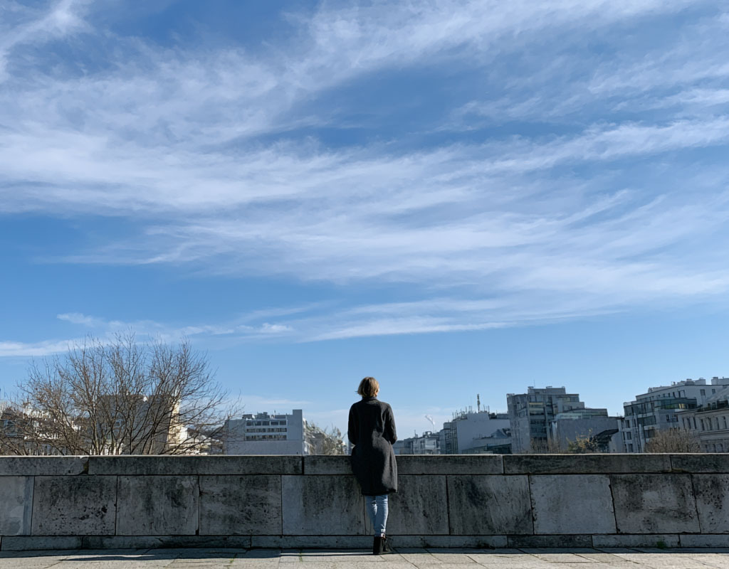 Silhouette einer Person, die in einer modernen Stadt steht und nach oben in den weiten, wolkenlosen Himmel blickt.
