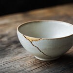 Handgefertigte Keramikschale mit feiner goldener Kintsugi-Reparaturlinie auf rustikalem Eichentisch