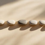 Geometrisch aufgereihte glatte Steine auf hellem Grund, ein Stein weicht leicht von der perfekten Linie ab